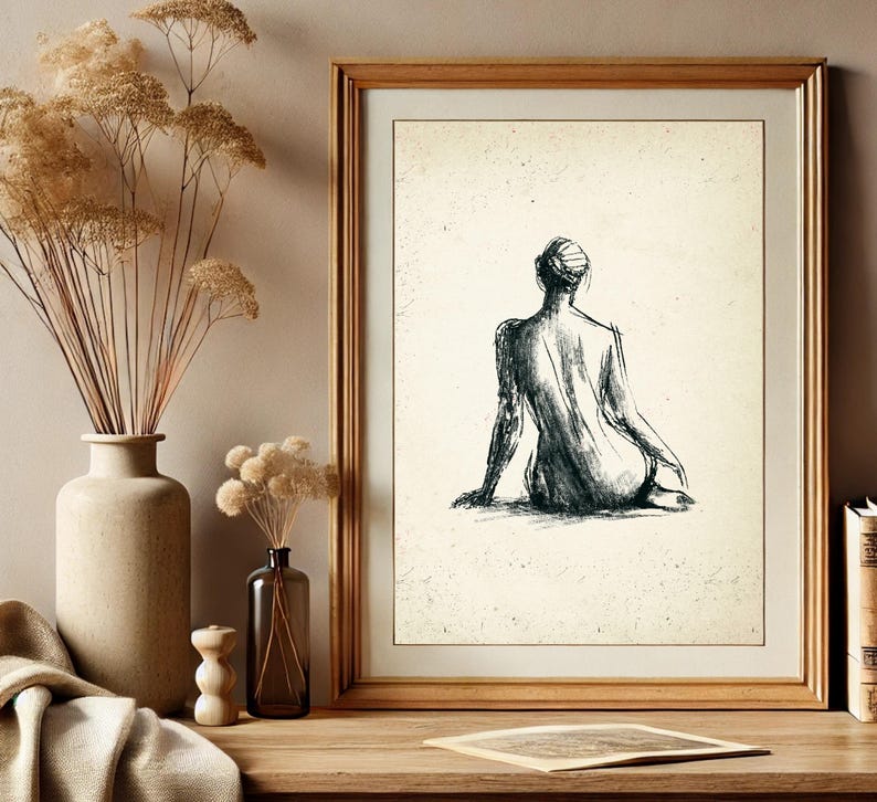 May include: A black and white line drawing of a person sitting with their back to the viewer. The drawing is framed in a light wood frame and is hanging on a wall.