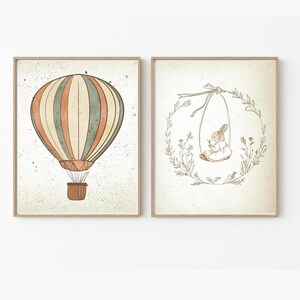 May include: Two framed prints, one with a hot air balloon with orange, green, and white stripes, and the other with a rabbit on a swing in a wreath of leaves.