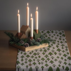 May include: A Christmas table decoration with four lit ivory candles in wooden holders. The arrangement includes pinecones and evergreen sprigs, on a wooden tray. A table runner with a green tree pattern completes the festive display.