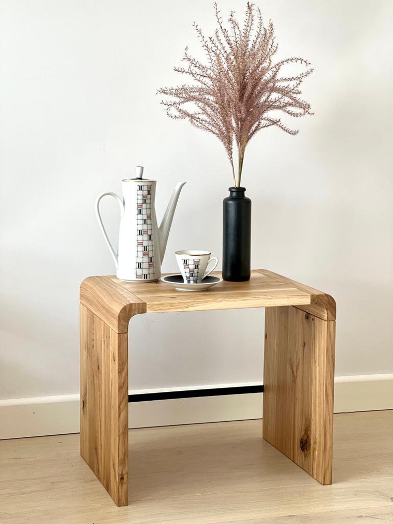 May include: A wooden side table with a curved design, featuring a white teapot, a small teacup and saucer, and a vase with dried pink pampas grass.