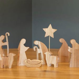 Puede incluir: Escena de la natividad de madera con figuras de María, José, el niño Jesús, un pastor, un ángel y dos ovejas. La escena también incluye una estrella y un pesebre.
