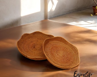 May include: Two woven wicker baskets with a natural brown color. The baskets are round and have a wavy edge. The baskets are on a wooden surface.