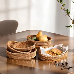 May include: Four woven wicker baskets in oval shapes, stacked on a wooden table. The top basket holds fruit, the second basket is empty, the third basket holds cookies, and the bottom basket is empty.
