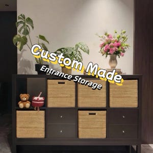 May include: A dark brown custom-made entrance storage unit with woven baskets and drawers. The unit is topped with plants and a vase of pink flowers. The text "Custom Made Entrance Storage" is displayed on the top of the unit.