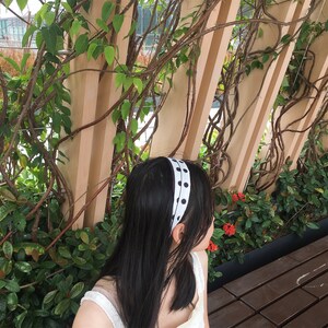 Pu&ograve; includere: Un cerchietto a pois bianco e nero con finitura in raso. Il cerchietto &egrave; indossato da una persona con lunghi capelli neri.