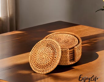 May include: Set of six woven rattan coasters in a natural brown color. The coasters are stacked in a circle and one coaster is lying on its side. The coasters are on a wooden table.