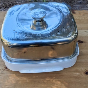 Puede incluir: Un calentador de alimentos cuadrado de plata con una base blanca y una perilla en la tapa que dice "HOT".