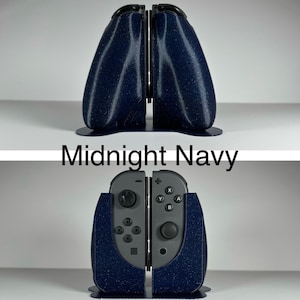 May include: A midnight navy blue 3D printed stand for two Nintendo Switch Joy-Con controllers. The stand is designed to hold the controllers upright and features a textured finish.