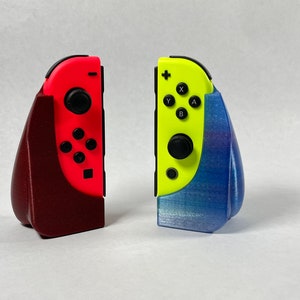 May include: Two Nintendo Switch Joy-Con controllers in red and yellow, each in a 3D printed stand. The red stand is maroon and the yellow stand is blue with a glittery finish.