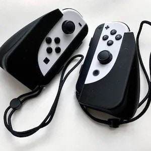 May include: Two black and white Nintendo Switch Joy-Con controllers with black silicone cases and wrist straps.