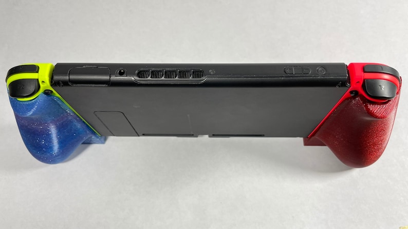 May include: A black Nintendo Switch console with a blue and green grip on the left side and a red grip on the right side.