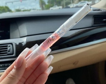 May include: A clear plastic tube with a pink liquid inside. The tube has a white cap and a white label with the word "Lip Oil" printed on it.