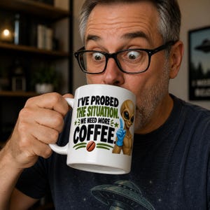 May include: A white ceramic mug featuring a graphic of a tan alien wearing a blue glove and the text I'VE PROBED THE SITUATION. WE NEED MORE COFFEE. The design includes green stars and a brown coffee bean illustration on the front of the mug.