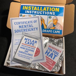 May include: A cardboard box containing a Certificate of Mental Sovereignty, a Mylar cape, and an adjustable tin foil hat. The box also includes installation instructions for the cape. The text on the items suggests protection from mind reading and surveillance.