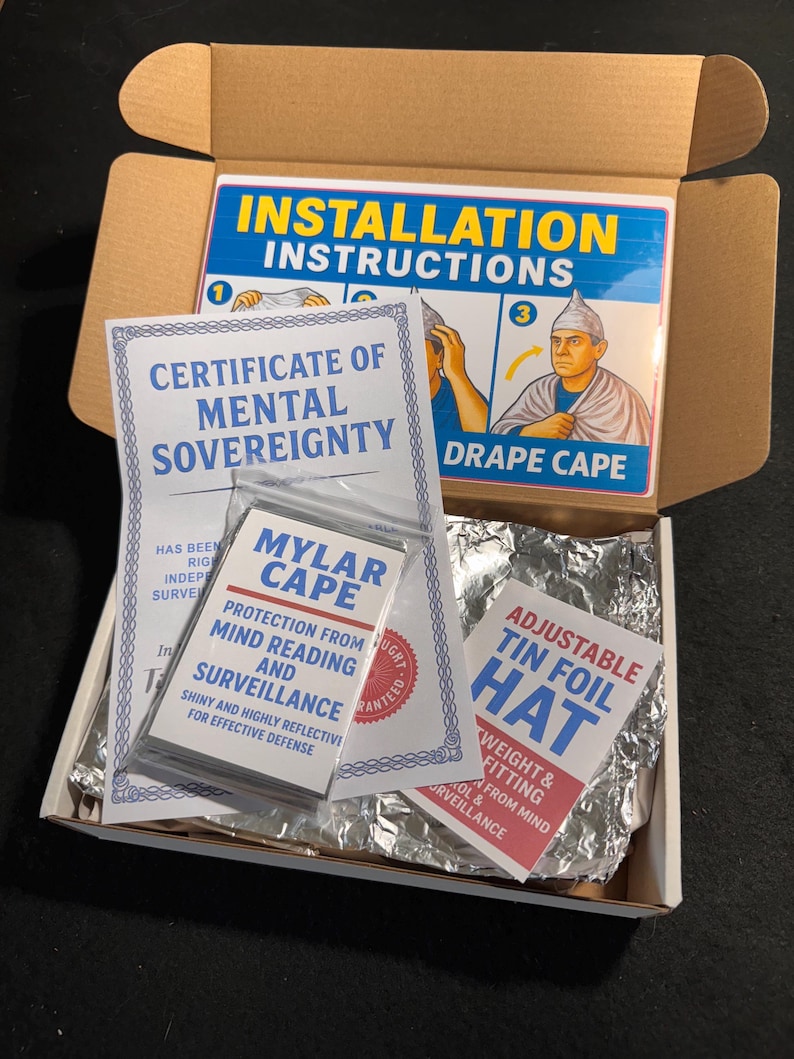 May include: A cardboard box containing a Certificate of Mental Sovereignty, a Mylar cape, and an adjustable tin foil hat. The box also includes installation instructions for the cape. The text on the items suggests protection from mind reading and surveillance.