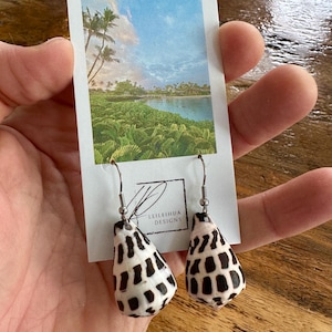 May include: A pair of earrings made from black and white patterned seashells with silver hooks. The earrings are displayed on a card with the text "Leileihu Designs".