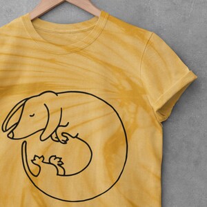 May include: A yellow tie-dye t-shirt with a black outline of a dachshund curled up sleeping.