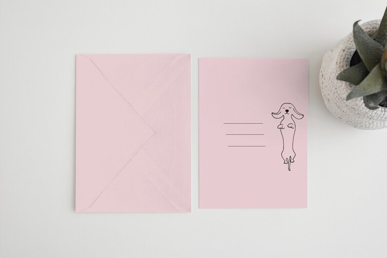 May include: A pink envelope with a blank pink card featuring a black line drawing of a dachshund standing on its hind legs.