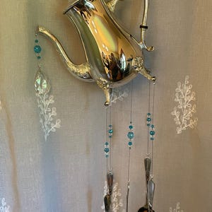 Puede incluir: Un carillón de tetera de plata con cuentas de vidrio azules y cucharas colgando.