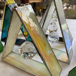 以下が含まれることがあります： 虹色のガラスとクリスタルプリズムが下からぶら下がった、3つのステンドグラスの三角形のサンキャッチャー。サンキャッチャーは、黄色、緑、青など、さまざまな色があります。