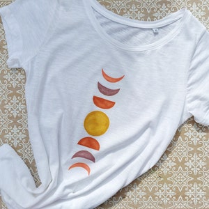 May include: White t-shirt with a graphic of a moon phases design in shades of orange, yellow, and purple.