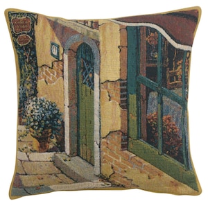 May include: A tapestry pillow featuring a detailed illustration of a building with a green door and window. The building is made of brick and has a yellow facade. The pillow has a gold border.