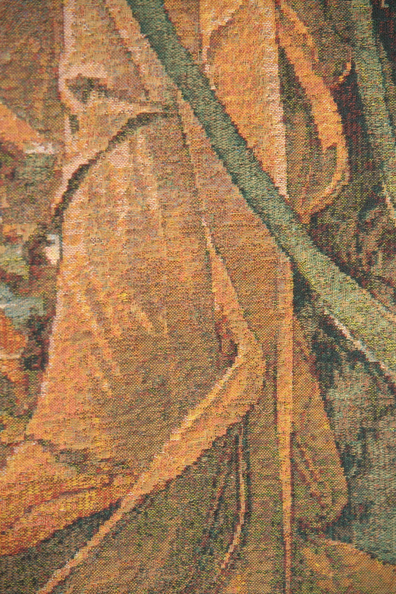 May include: Close-up of a woven tapestry with a detailed, textured design. The tapestry features a blend of warm colors, including shades of brown, orange, and green, creating a natural, earthy aesthetic. The pattern appears to depict abstract foliage.