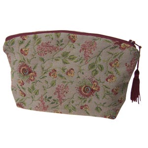 May include: A beige tapestry cosmetic bag with a floral pattern in shades of red, pink, and green. The bag has a burgundy zipper and a matching tassel. The bag is designed to hold makeup and other beauty products.