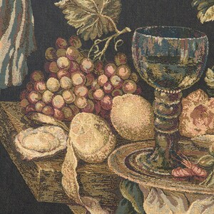 May include: A still life tapestry featuring a dark background with a wooden table, a glass of wine, grapes, lemons, and a white cloth.