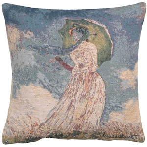 May include: A tapestry pillow featuring a woman in a white dress holding a green umbrella, walking in a field with a blue sky and white clouds. The pillow has the artist's signature, Claude Monet, in the bottom right corner.