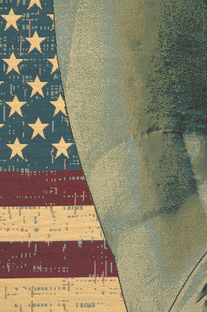 May include: A close-up of a tapestry featuring a faded American flag with red, white and blue stripes and yellow stars. The flag is partially obscured by a textured, beige background.