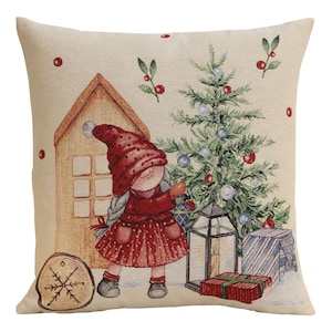 May include: A decorative square pillow with a Christmas theme. The pillow features a whimsical illustration of a girl in a red outfit, a Christmas tree, a house, and wrapped gifts. The color palette includes red, green, and beige.
