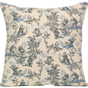 May include: A cream-colored throw pillow with a blue and white floral pattern. The pattern features small figures of people in a garden setting.