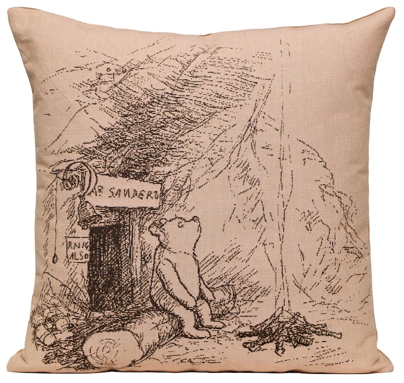 A tapestry cushion featuring an image of Winnie-the-Pooh sitting on a log in front of a campfire. Colors are beige and dark brown.