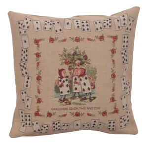 May include: A beige throw pillow with a tapestry design featuring three playing card characters from Alice in Wonderland. The characters are standing in front of a tree with white flowers. The border of the pillow is a repeating pattern of playing cards and red roses.