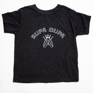 May include: A dark gray t-shirt with a white graphic of a fly and the text "SUPA DUPA" in a collegiate font.