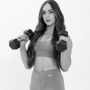May include: A woman wearing a black sports bra and black leggings with a white logo that says "Rise" is lifting weights. She is looking at the camera.