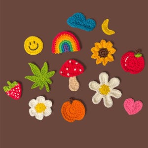 Puede incluir: Una colecci&oacute;n de peque&ntilde;as aplicaciones de ganchillo coloridas que incluyen una cara sonriente amarilla, un arco&iacute;ris, una nube azul, una luna creciente amarilla, un girasol, una manzana roja, una fresa, una hoja verde, una seta roja, dos flores blancas, una naranja y un coraz&oacute;n rosa.