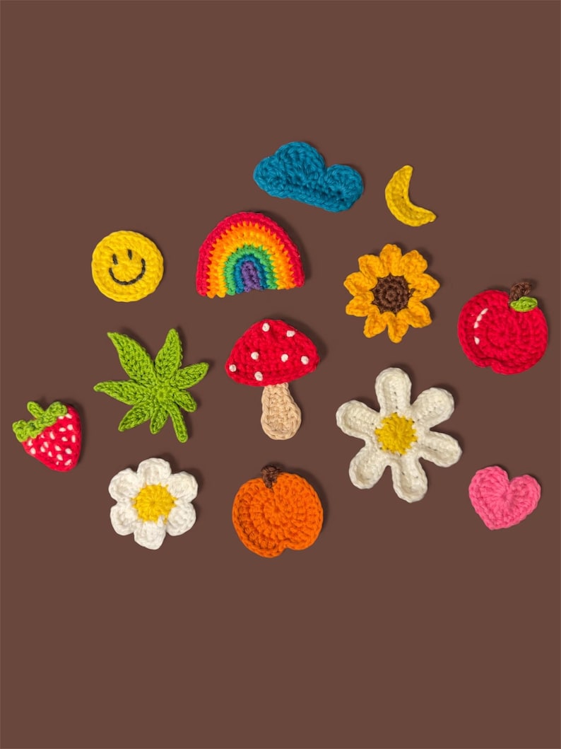 Puede incluir: Una colecci&oacute;n de peque&ntilde;as aplicaciones de ganchillo coloridas que incluyen una cara sonriente amarilla, un arco&iacute;ris, una nube azul, una luna creciente amarilla, un girasol, una manzana roja, una fresa, una hoja verde, una seta roja, dos flores blancas, una naranja y un coraz&oacute;n rosa.