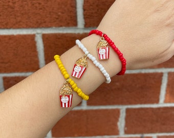 May include: Three beaded bracelets with popcorn charm pendants. The bracelets are red, white, and yellow.