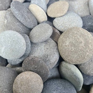 May include: A collection of smooth, rounded river rocks in various shades of gray, beige, and brown. The stones vary in size and shape, creating a natural, textured appearance. Ideal for landscaping or decorative purposes.