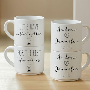 May include: Two white ceramic mugs stacked on top of each other. The top mug says "Let's have coffee together" with a small heart and coffee cup graphic. The bottom mug says "For the rest of our lives" with a small heart and coffee cup graphic. Two more white ceramic mugs are stacked on top of each other. The top mug says "Andrew Jennifer EST. 2024" with a small heart graphic. The bottom mug says "Andrew Jennifer EST. 2024" with a small heart graphic.