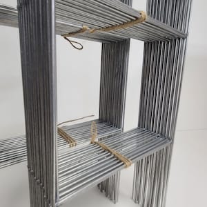May include: A metal shelf unit made of multiple thin metal rods, tied together with twine. The shelf unit has three shelves.
