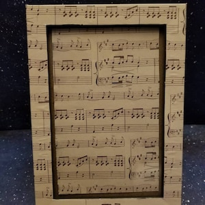 May include: A picture frame with a brown border and a beige background. The frame is decorated with a pattern of musical notes.