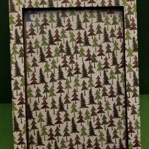 May include: A white picture frame with a brown inner border. The frame has a pattern of green and brown trees printed on the surface.