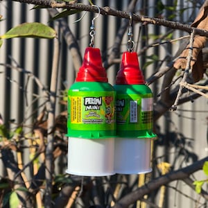 May include: A pair of novelty earrings made from Pelon Mini candy containers. The earrings feature red and green tops, white bases, and silver-colored ear wires. The candy containers have text and graphics.