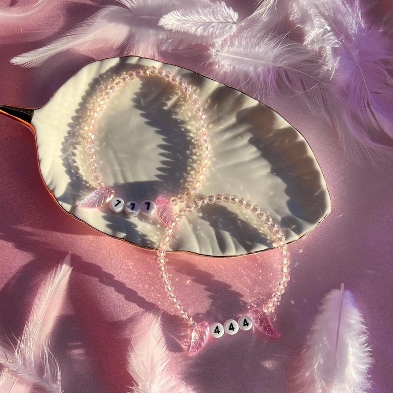May include: Two pink beaded bracelets with angel wing charms. The charms have the numbers 717 and 444 on them.