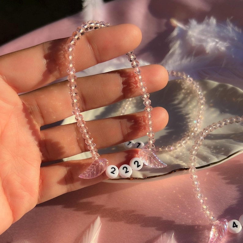 May include: A pink and clear beaded necklace with pink angel wing charms and white beads with the numbers 222.