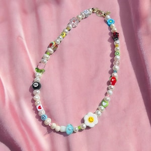 Puede incluir: Un collar de perlas blancas con abalorios coloridos, incluyendo una cara sonriente, un signo de paz, un corazón, una mariquita, una flor, un dado y una bola de billar 8.