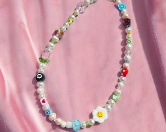 May include: A white pearl necklace with colorful charms, including a smiley face, a peace sign, a heart, a ladybug, a flower, a dice, and a 8 ball.